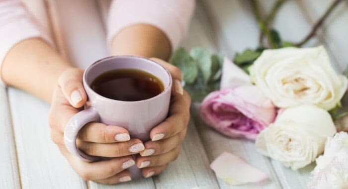 Kvinde holder en kop te på et bord med blomster